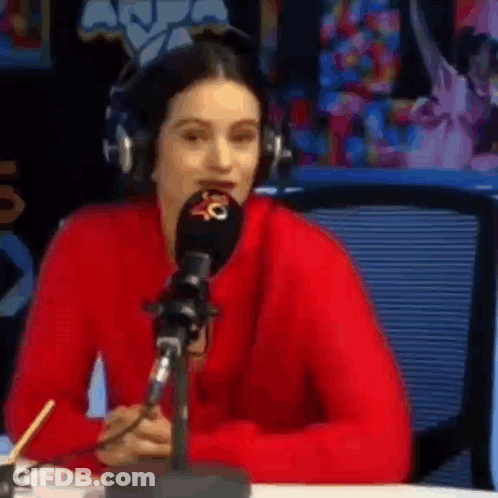 A Woman In A Red Sweater Is Sitting At A Table In Front Of A Microphone . GIF