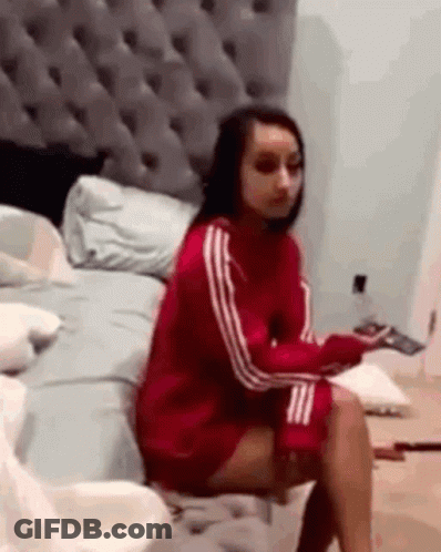 A Woman In A Red Sweater Is Sitting On A Bed . GIF