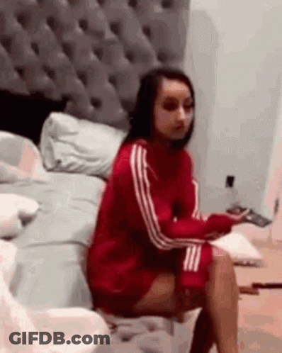 A Woman In A Red Sweater Is Sitting On A Bed With Her Legs Crossed . GIF