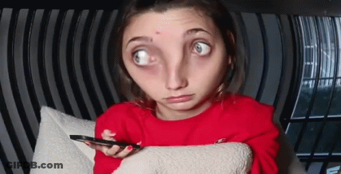 A Woman In A Red Sweater Is Sitting On A Couch Holding A Cell Phone And Making A Funny Face . GIF