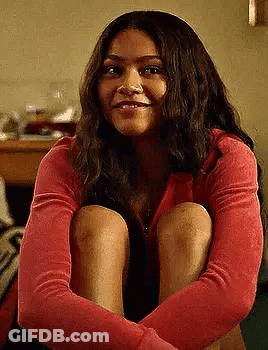 A Woman In A Red Sweater Is Sitting On The Floor With Her Legs Crossed . GIF