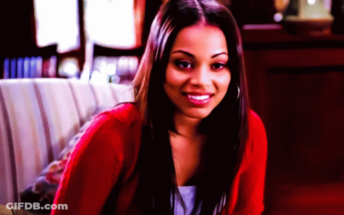 A Woman In A Red Sweater Is Smiling And Looking At The Camera GIF
