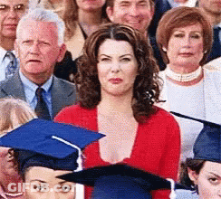 A Woman In A Red Sweater Is Standing In Front Of A Crowd Of People Wearing Graduation Caps . GIF