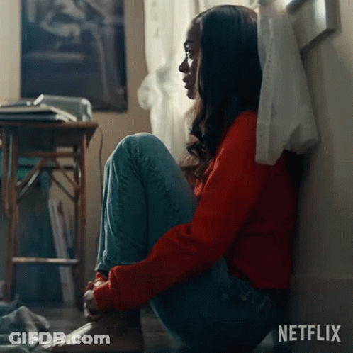 A Woman In A Red Sweater Sits On The Floor In Front Of A Netflix Sign GIF