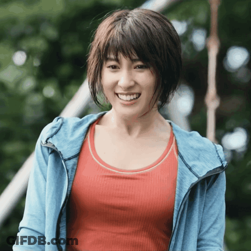 A Woman In A Red Tank Top And A Blue Jacket Smiles For The Camera GIF