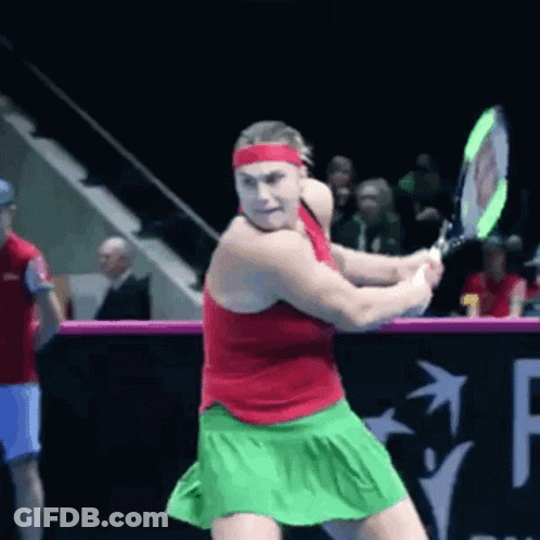 A Woman In A Red Tank Top And Green Skirt Is Swinging A Tennis Racket GIF