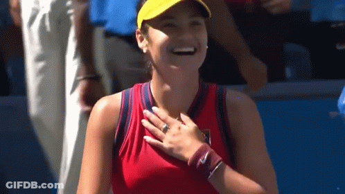 A Woman In A Red Tank Top And Yellow Hat Is Smiling And Holding Her Hand To Her Chest . GIF