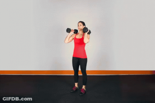 A Woman In A Red Tank Top Is Holding A Pair Of Dumbbells Over Her Head GIF