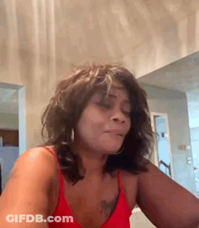 A Woman In A Red Tank Top Is Sitting In Front Of A Mirror . GIF