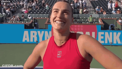 A Woman In A Red Tank Top Is Smiling In Front Of A Banner That Says " Aryn " GIF