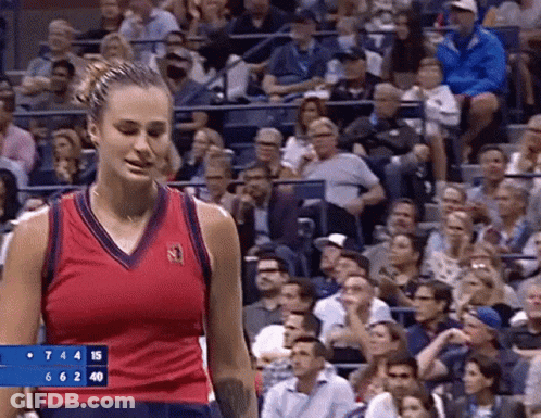 A Woman In A Red Tank Top Is Standing In Front Of A Crowd At A Tennis Game . GIF