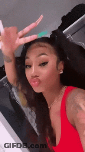 A Woman In A Red Tank Top Is Taking A Selfie In A Mirror . GIF