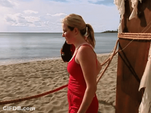 A Woman In A Red Tank Top Stands On A Beach GIF