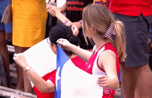A Woman In A Red Tank Top With The Word Hero On It Holds A Flag GIF