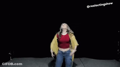 A Woman In A Red Top And A Yellow Jacket Is Dancing On A Stage With Her Arms In The Air . GIF