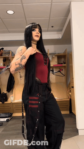 A Woman In A Red Top And Black Pants Is Standing In A Room GIF