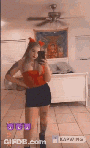 A Woman In A Red Top And Black Skirt Is Taking A Picture Of Herself In A Mirror . GIF