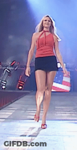 A Woman In A Red Top And Black Skirt Is Walking Down A Stage GIF