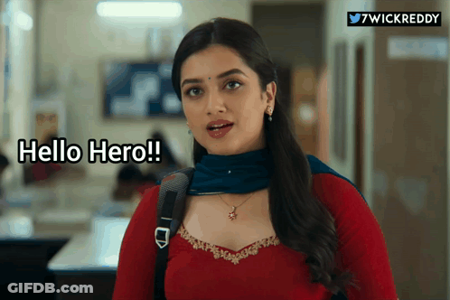 A Woman In A Red Top And Blue Scarf Is Standing In A Hallway And Says Hello Hero GIF