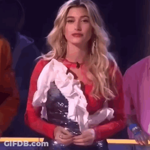A Woman In A Red Top And White Ruffled Skirt Is Standing In Front Of A Crowd . GIF