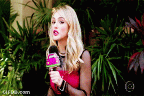 A Woman In A Red Top Is Holding A Microphone In Front Of Plants GIF