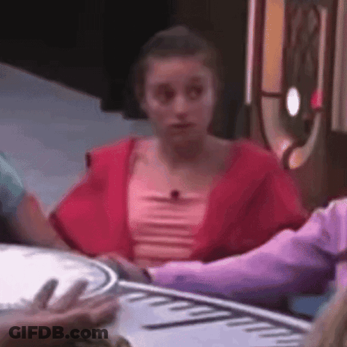 A Woman In A Red Top Is Sitting At A Table With A Clock On It . GIF