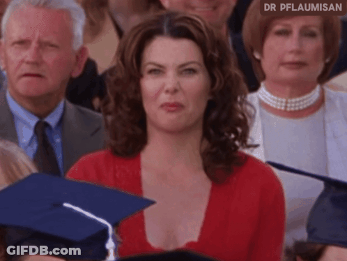 A Woman In A Red Top Is Sitting In A Crowd Of People With A Graduation Cap On . GIF