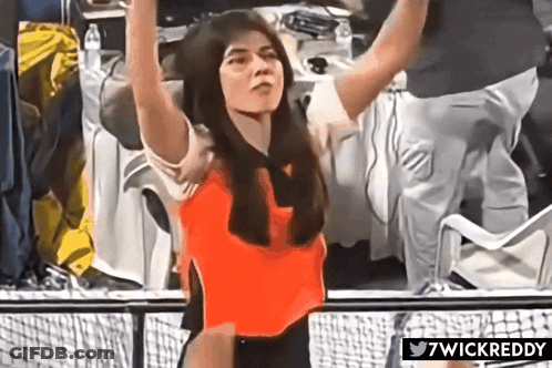 A Woman In A Red Top Is Standing In Front Of A Fence With 7Wickreddy Written Below Her GIF