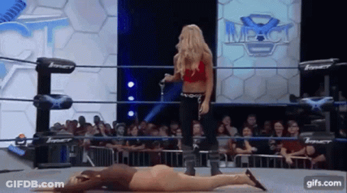 A Woman In A Red Top Is Standing Next To A Woman Laying On The Ground . GIF
