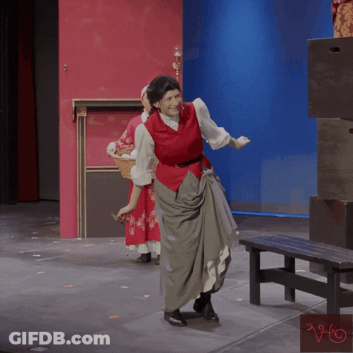 A Woman In A Red Vest Stands On A Stage GIF