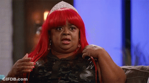 A Woman In A Red Wig And Tiara Is Sitting On A Couch . GIF