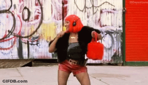 A Woman In A Red Wig Is Holding A Red Purse In Front Of A Graffiti Wall .. GIF