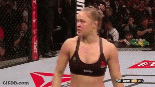 A Woman In A Reebok Bra Is Standing In A Cage During A Ufc Fight . GIF