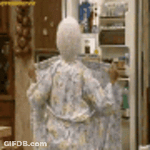 A Woman In A Robe Is Standing In Front Of A Refrigerator In A Kitchen . GIF