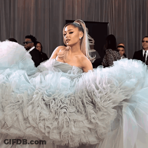 A Woman In A Ruffled Dress Stands In Front Of A Group Of Men GIF