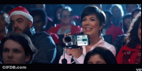 A Woman In A Santa Hat Is Holding A Video Camera GIF