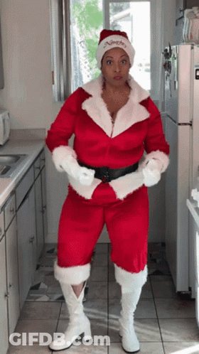 A Woman In A Santa Suit Is Standing In Front Of A White Refrigerator GIF