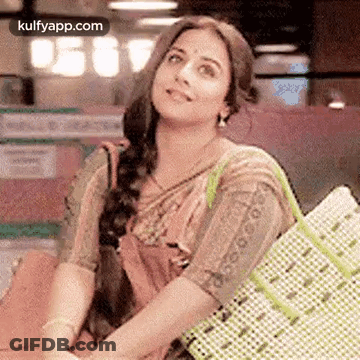 A Woman In A Saree Is Holding A Shopping Bag And Smiling While Sitting Down . GIF
