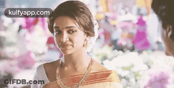 A Woman In A Sari Is Standing Next To A Man In A Room And Smiling . GIF