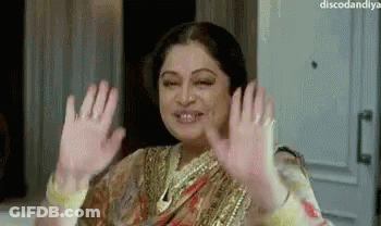 A Woman In A Sari Is Waving Her Hands In The Air And Smiling . GIF