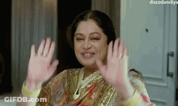 A Woman In A Sari Is Waving Her Hands In The Air And Smiling . GIF