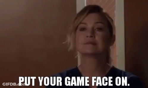 A Woman In A Scrub Top Is Standing In Front Of A Door And Says `` Put Your Game Face On . '' GIF