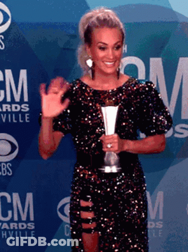 A Woman In A Sequined Dress Is Holding A Trophy In Front Of A Wall That Says Cm Awards GIF