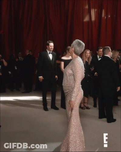 A Woman In A Sequined Dress Is Kissing A Man In A Tuxedo On A Red Carpet GIF