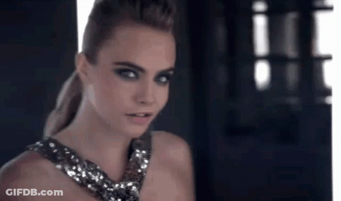 A Woman In A Sequined Dress Is Standing In Front Of A Window Looking At The Camera . GIF