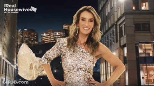 A Woman In A Sequined Dress Stands In Front Of A Real Housewives Poster GIF