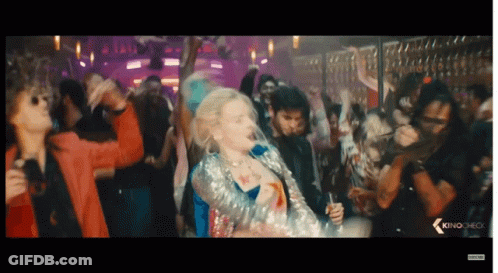 A Woman In A Sequined Jacket Is Dancing In Front Of A Crowd With The Word Kino On The Bottom Left GIF