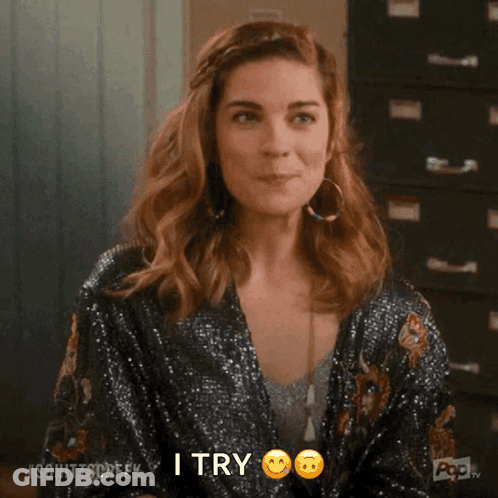 A Woman In A Sequined Jacket Is Smiling And Making A Peace Sign With Her Finger . GIF