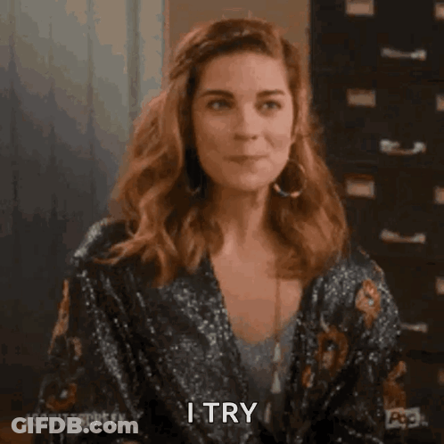 A Woman In A Sequined Jacket Is Smiling And Saying `` I Try '' While Holding Her Hair . GIF