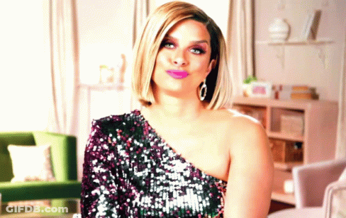A Woman In A Sequined One Shoulder Dress Is Sitting In A Living Room GIF